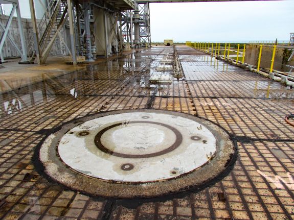 Large-format photograph: Pad Deck, Launch Complex 39-B, showing Apollo Era Crawlerway Grid Panels west of Flame Trench in area south of Side Flame Deflector Service/Park Positions Transport Rails. By the time this photograph was taken, the RSS and FSS had both been demolished and removed in preparations for the Artemis Program. Visible on left is the underside of the MLP Utilities Interface Platform, which did not get removed. In the foreground, the round outline of an Extensible Columns Foundation Interface Plate (6” thick steel) can be seen. Photo credit: Withheld by request.